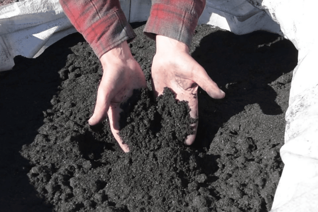 A photograph of two hands holding rich, dark soil.